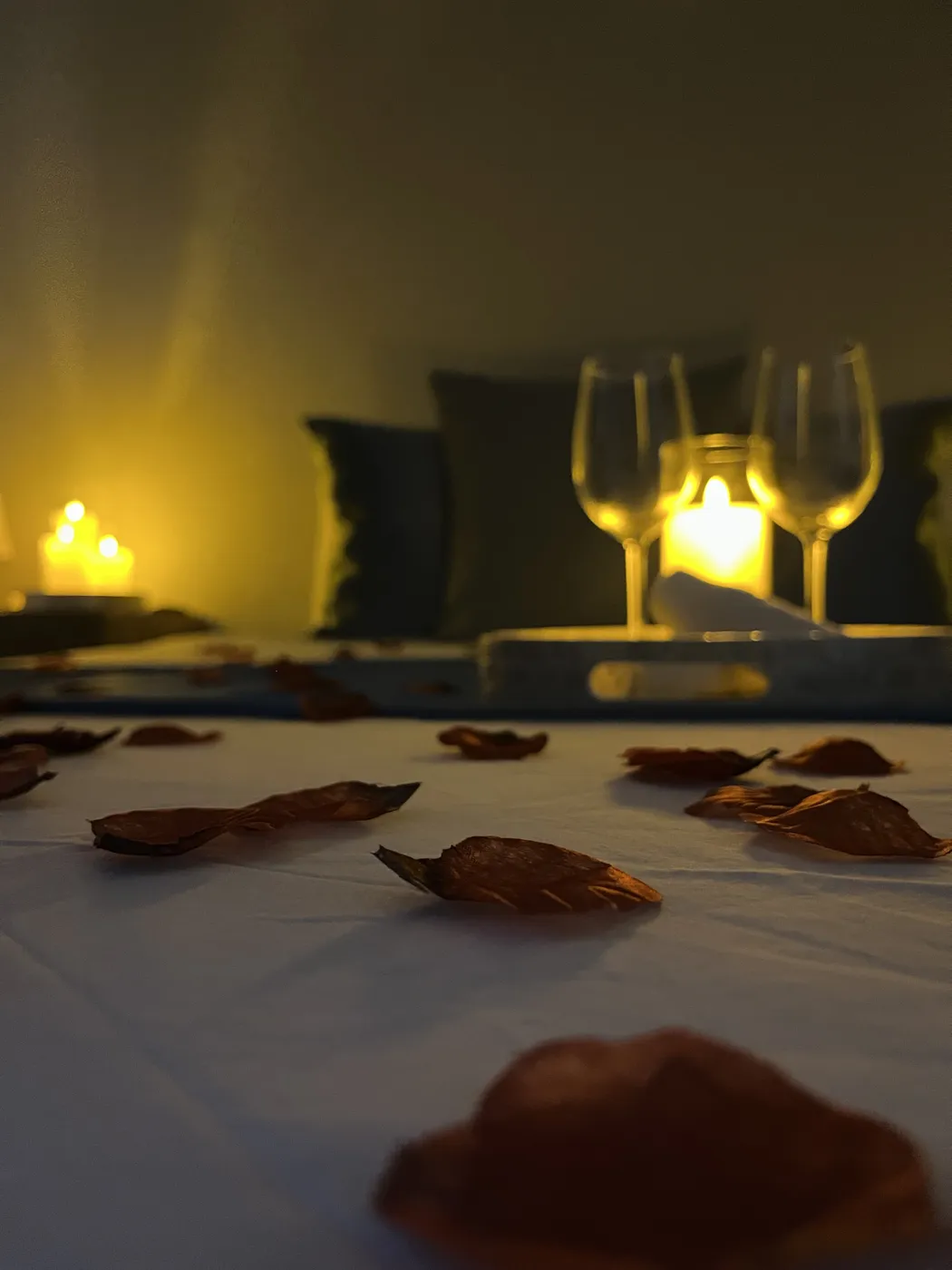 Pétales de rose sur le lit, verres et bougies en arrière-plan